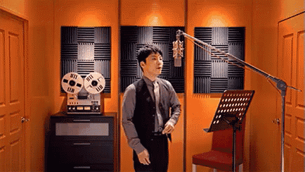 a man is standing in front of a microphone in a recording studio with an orange wall .