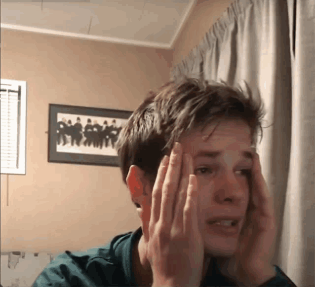 a young man holds his head in front of a framed picture