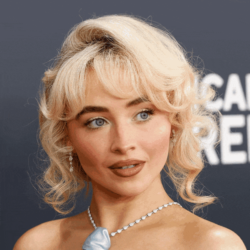 a woman with blonde hair and blue eyes is wearing a blue necklace