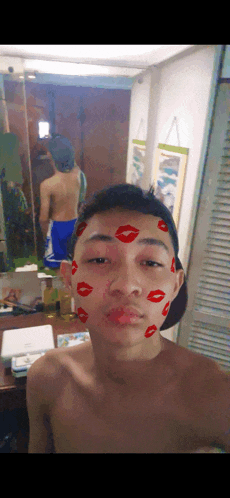 a shirtless man is taking a selfie with red kisses on his face