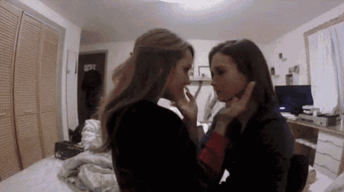 two women are kissing in a bedroom in front of a bed .