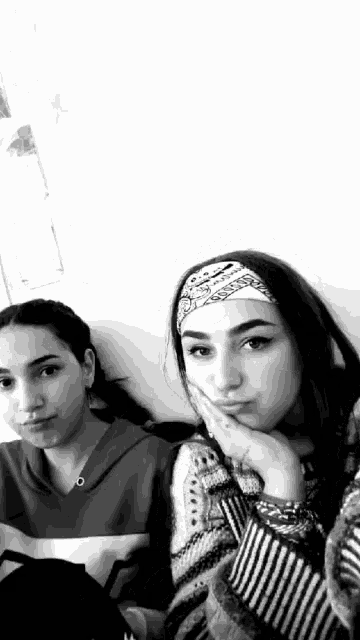 two girls are posing for a picture together in a black and white photo . one girl is wearing a headband .