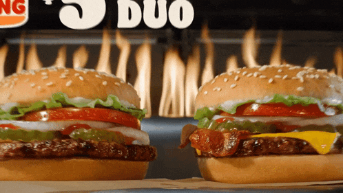 two burger king hamburgers are on a table in front of a fire