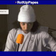 a man wearing a white beanie is talking into an orange microphone with the words rolluppapes in the corner
