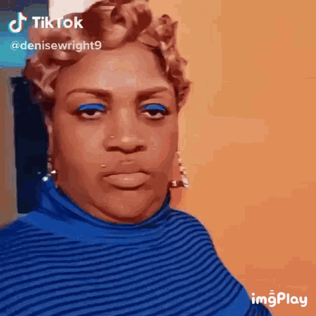 a woman with blue eye shadow and a blue sweater is making a funny face .