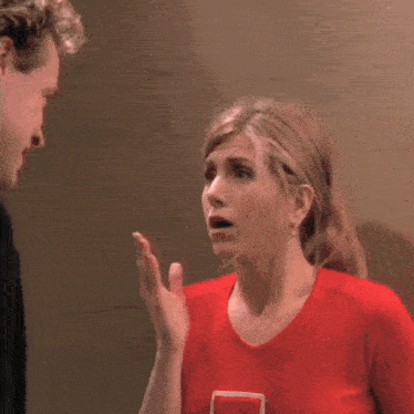 a woman in a red shirt with a white square on it talks to a man