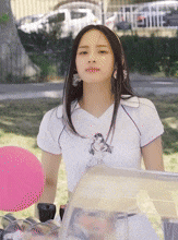 a woman in a white shirt is standing next to a pink balloon in a park