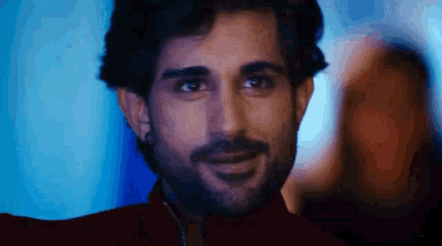 a man with a beard is smiling in front of a blue background