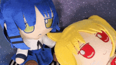 two stuffed dolls one with blue hair and one with yellow hair are laying next to each other