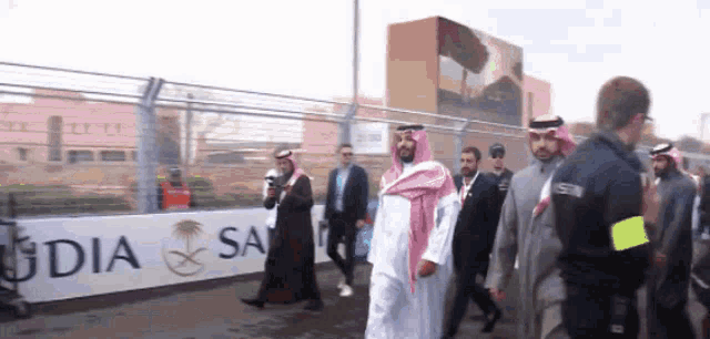a group of men are walking in front of a sign that says saudi arabia