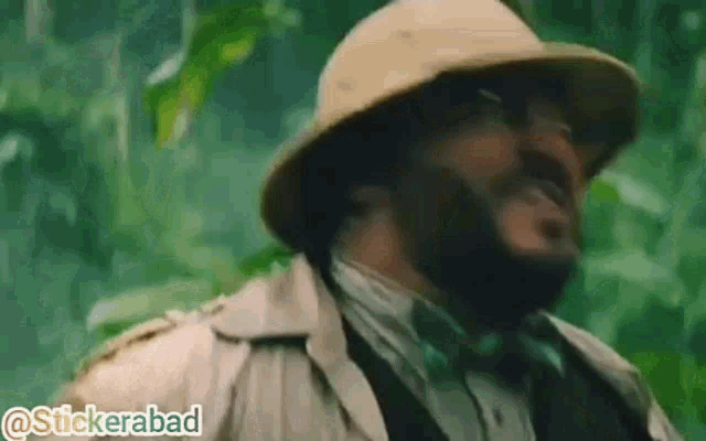 a man with a beard wearing a hat and glasses is in the jungle .