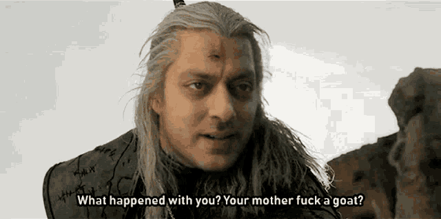 a man with long hair and a scar on his forehead is talking to someone .
