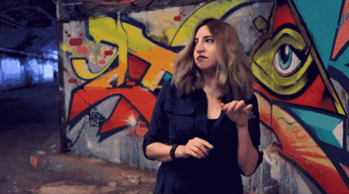 a woman stands in front of a wall with graffiti on it including the word jc
