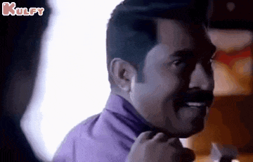 a man with a mustache and a purple shirt is smiling while talking to another man .
