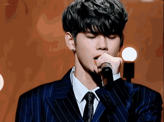 a young man in a suit and tie sings into a microphone