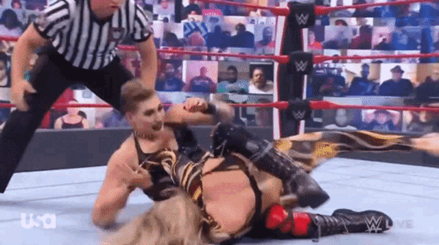 a wrestler is laying on the ground in a wrestling ring while a referee looks on .