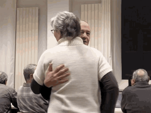 a woman in a white sweater is hugging a man in a black shirt