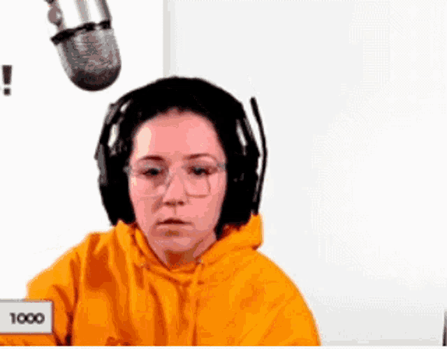 a woman wearing headphones and an orange hoodie is sitting in front of a microphone .