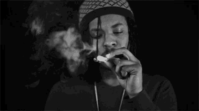 a man with dreadlocks is smoking a cigarette in a black and white photo