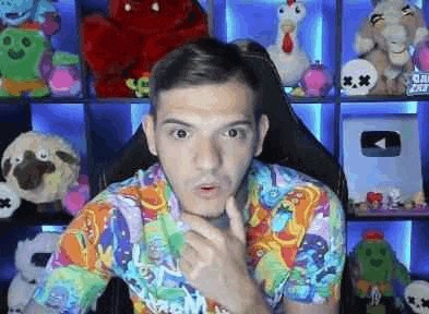 a man in a colorful shirt is sitting in a chair in front of a shelf filled with stuffed animals .