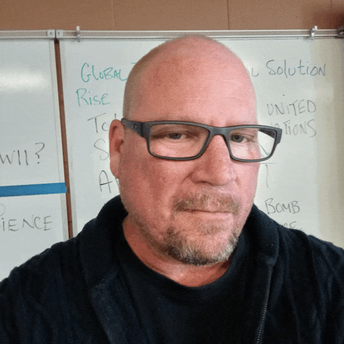 a bald man wearing glasses stands in front of a white board that says global rise on it
