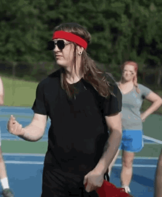 a man wearing sunglasses and a red headband is dancing on a tennis court