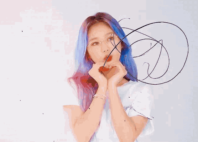 a woman with blue hair is making a heart shape with her hands .