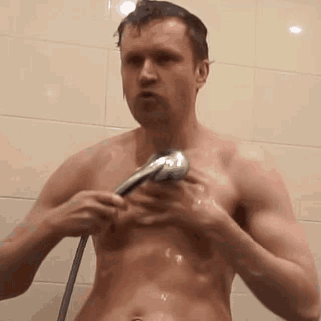 a shirtless man is taking a shower and holding a shower head .