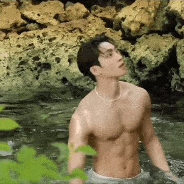 a shirtless man is standing in a body of water next to rocks .