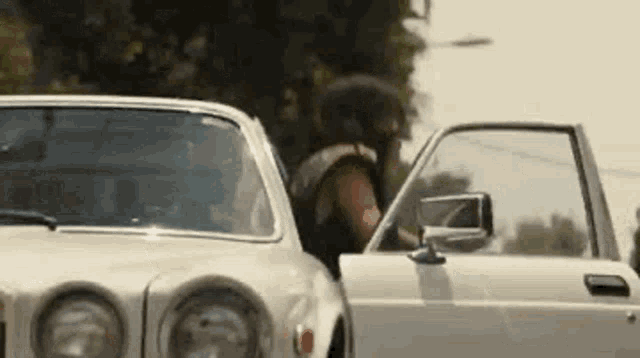 a man is getting out of a white car with his door open .