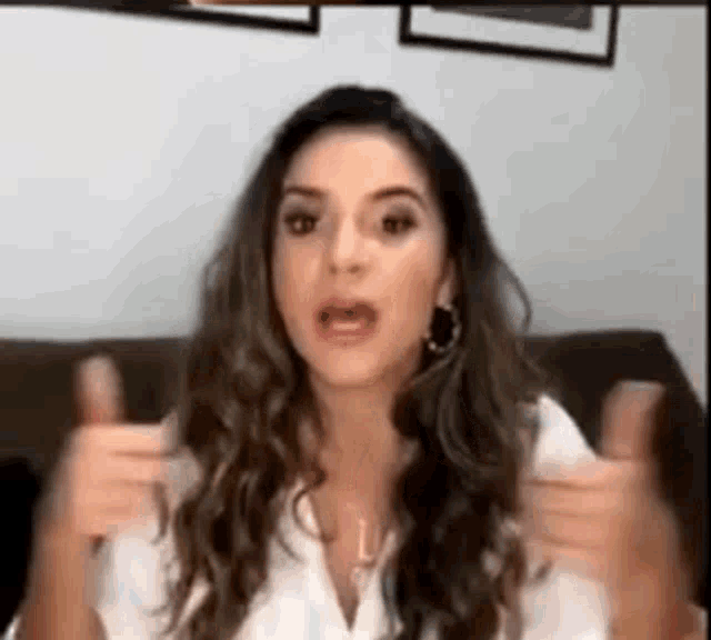 a woman in a white shirt is sitting on a couch making a funny face .