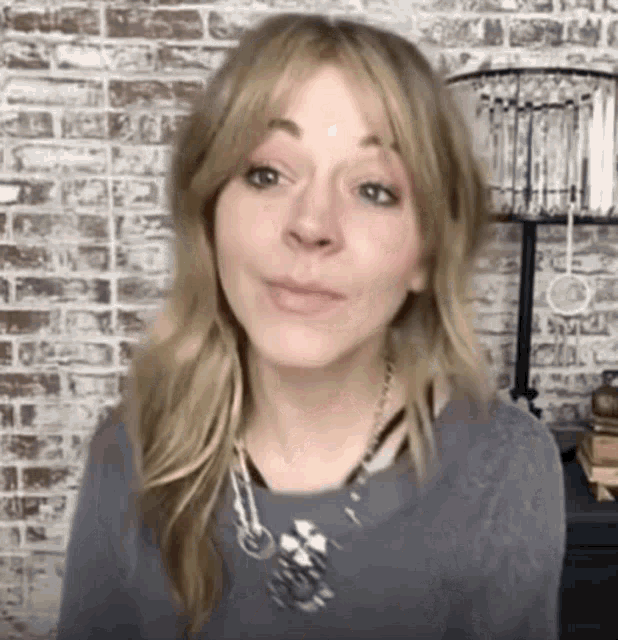 a woman is standing in front of a brick wall wearing a necklace and a sweater .
