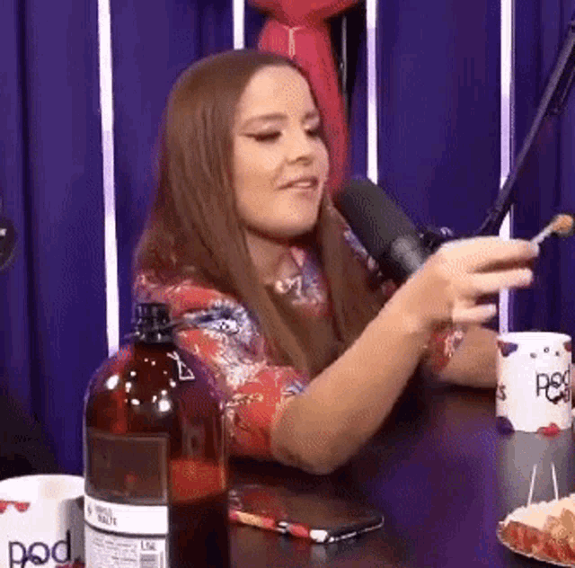 a woman is sitting at a table in front of a microphone holding a spoon .
