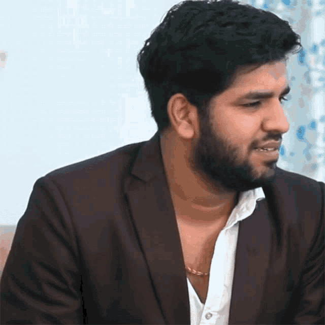 a man with a beard wearing a brown jacket and a white shirt