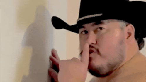 a man wearing a cowboy hat is holding his finger to his mouth .