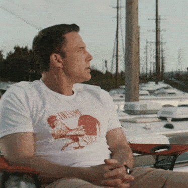 a man wearing an awesome sauce shirt sits on a chair
