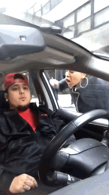 a man in a red hat is sitting in a car with a woman yelling at him