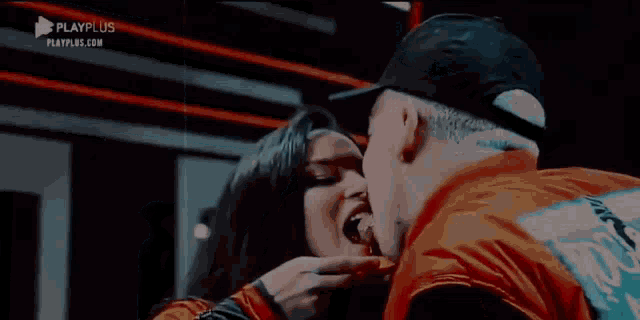 a man and a woman are kissing in front of a sign that says playplus