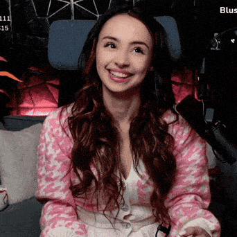 a woman in a pink sweater is smiling in front of a microphone with the word blus on the bottom