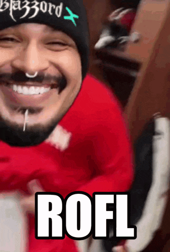 a man wearing a red shirt and a black beanie is smiling and says rofl