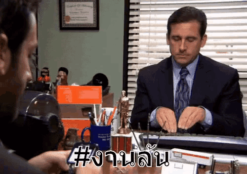 a man in a suit and tie is typing on a keyboard while another man looks on .