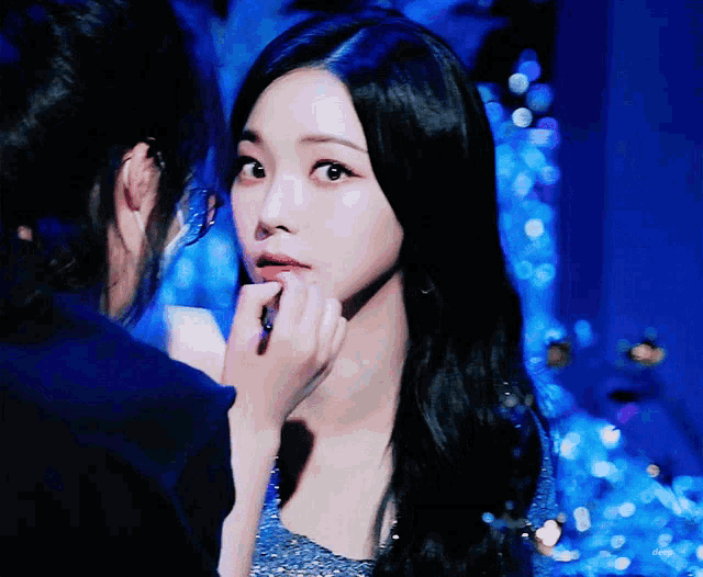 a woman is touching another woman 's face in a blue room