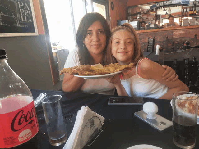 two women sitting at a table with a coca cola bottle in front of them