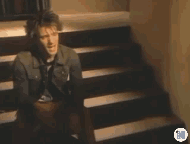a man is sitting on a set of stairs with the letter n in the corner