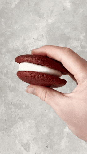 a hand is holding a red velvet sandwich cookie