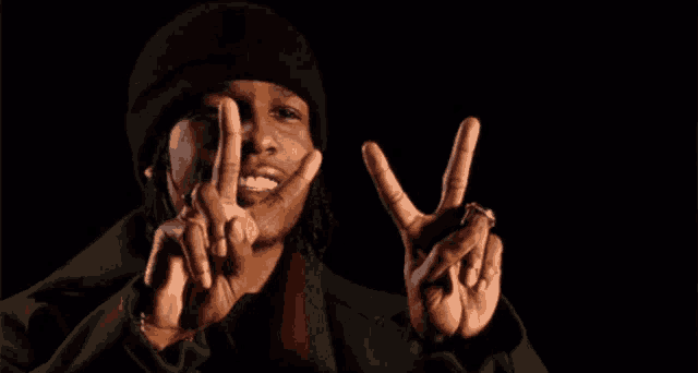 a man wearing a hat and a scarf is making a peace sign with his hands .