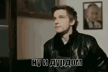a man in a leather jacket is standing in front of a painting of a man .