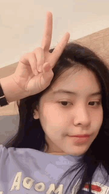 a girl in a purple shirt is making a peace sign with her fingers