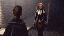 a woman in a black outfit is holding a sword and talking to another woman
