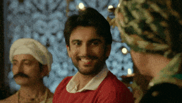 a man in a red shirt is smiling in front of a group of men